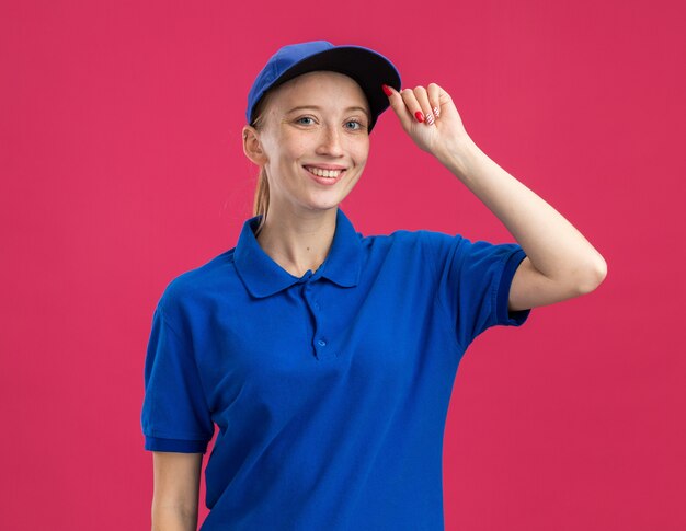 Happy young delivery girl in blue uniform and cap   smiling confident