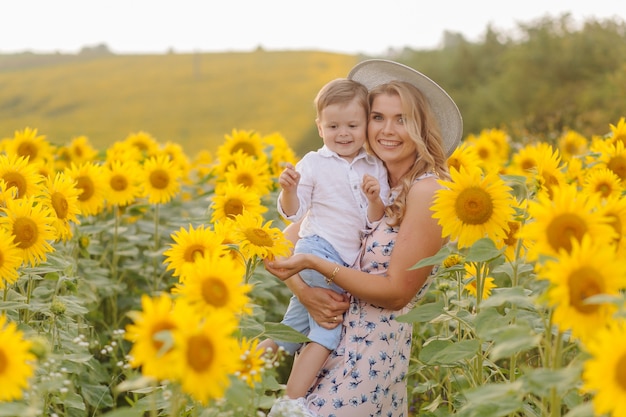 Happy young family, mother father and son, are smiling, holding and hugging in the sunflower field