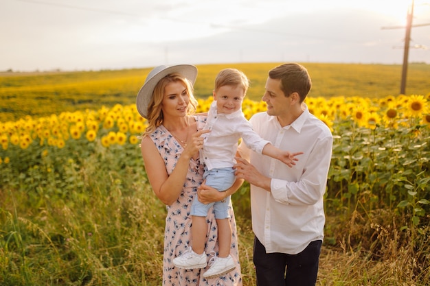 Happy young family, mother father and son, are smiling, holding and hugging in the sunflower field