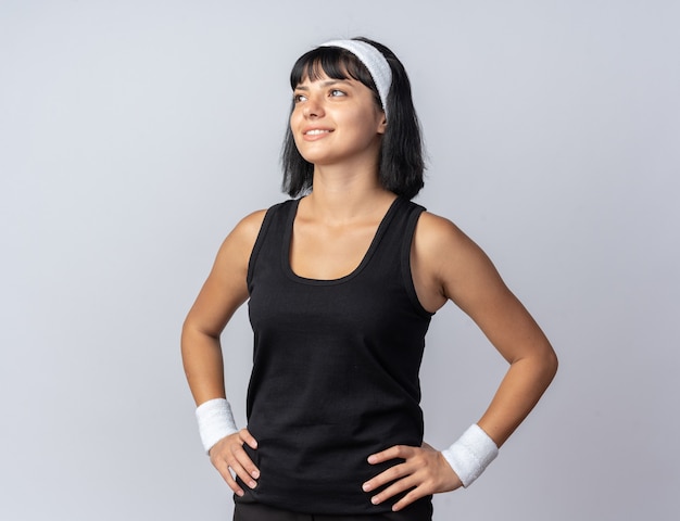 Free photo happy young fitness girl wearing headband looking up smiling cheerfully standing over white background