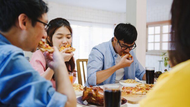 Happy young friends group having lunch at home. Asia family party eating pizza food and laughing enjoying meal while sitting at dining table together at house. Celebration holiday and togetherness.