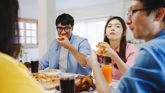 Happy young friends group having lunch at home. Asia family party eating pizza food and laughing enjoying meal while sitting at dining table together at house. Celebration holiday and togetherness.