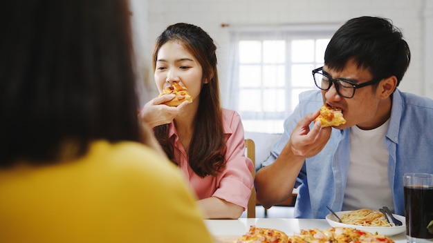 Happy young friends group having lunch at home. Asia family party eating pizza food and laughing enjoying meal while sitting at dining table together at house. Celebration holiday and togetherness.