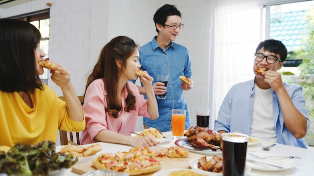 Happy young friends group having lunch at home. Asia family party eating pizza food and laughing enjoying meal while sitting at dining table together at house. Celebration holiday and togetherness.