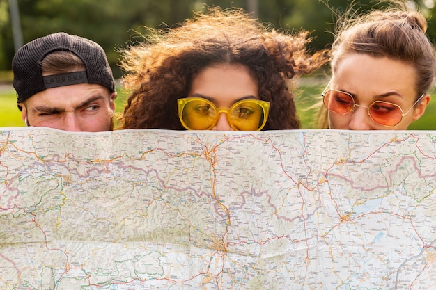 Free photo happy young funny company of friends tourists hiding behind map in sunglasses, man and women having fun together, traveling