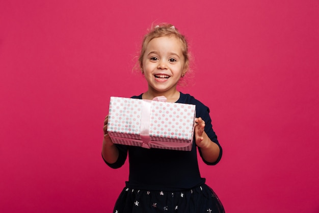 Happy young girl holding gift box and looking at camera