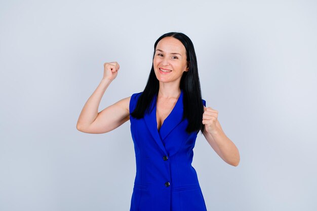 Happy young girl is looking at camera by raising up her fists on white background