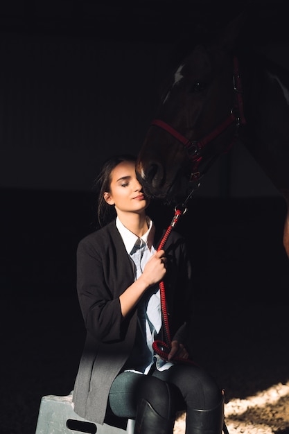 Free photo happy young girl sitting outdoors hugging her horse