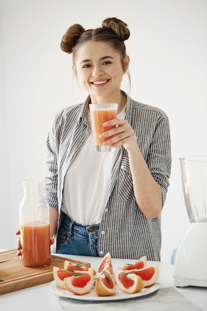 Free photo happy young girl smiling holding glass with healthy detox grapefruit smoothie over white wall.