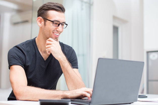 Free photo happy young handsome man working on laptop