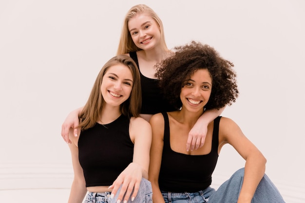 Happy young interracial beauty girls in tops and jeans smiling looking at camera on white background