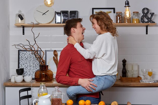 Happy young lovely couple on kitchen hugging each other. They enjoy spending time togehter. The man holding his girlfriend