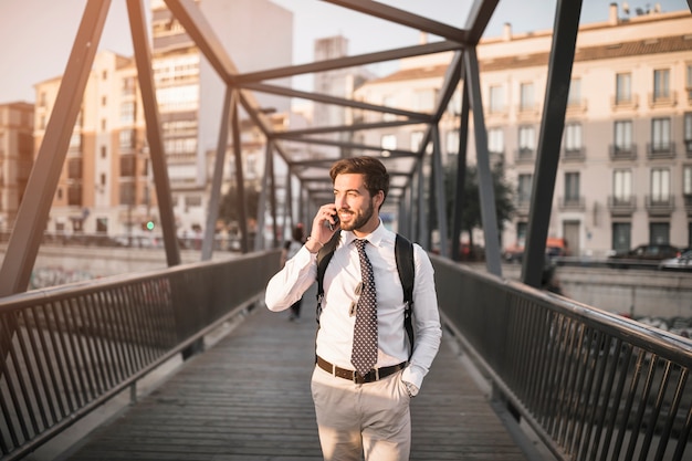 Happy young male travel standing on bridge talking on cellphone