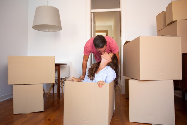 Happy young man dragging box with his girlfriend inside and kissing her