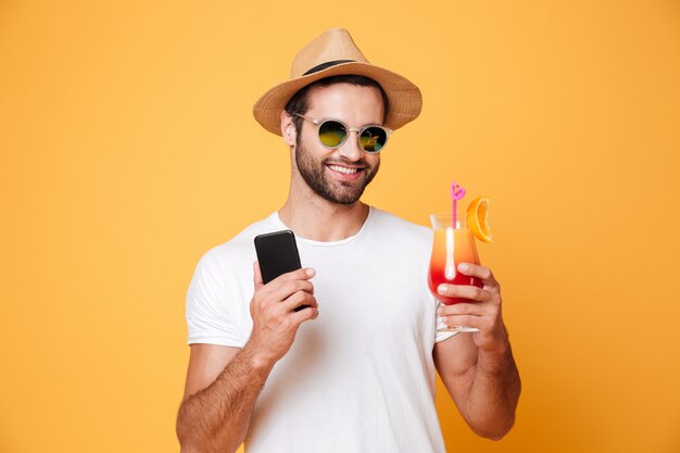 Happy young man holding mobile phone and cocktail