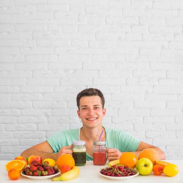 Happy young man holding smoothies with colorful fresh organic fruits on desk