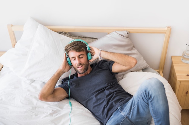 Free Photo happy young man listening music on the bed