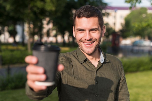 Happy young man showing disposable coffee cup at park