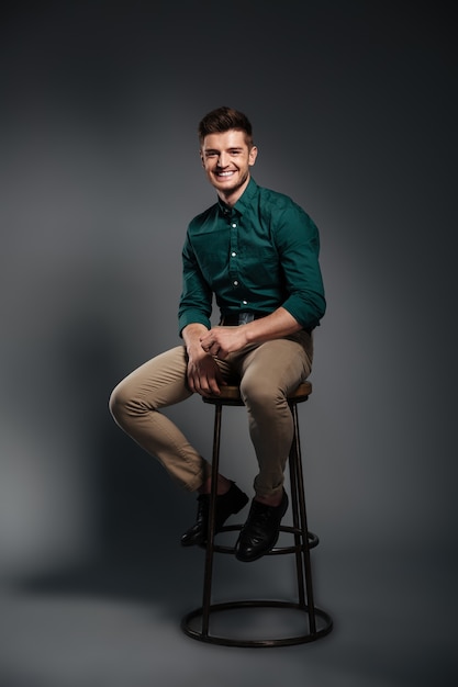 Happy young man sitting isolated over grey