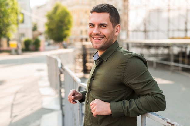 Happy young man standing near metallic railing looking at camera