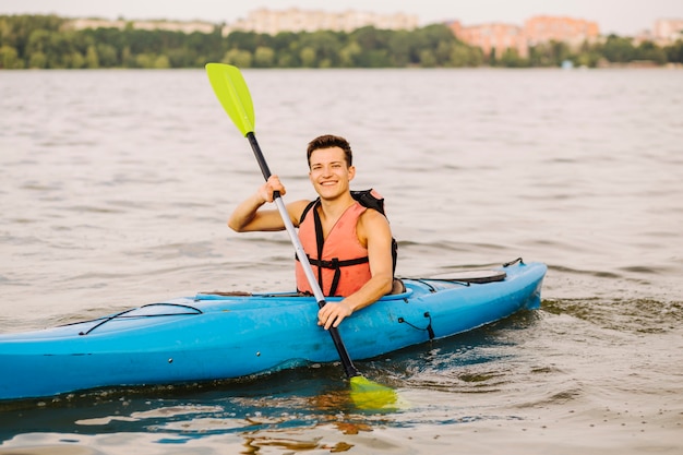 Free Photo happy young man using paddle kayaking on lake