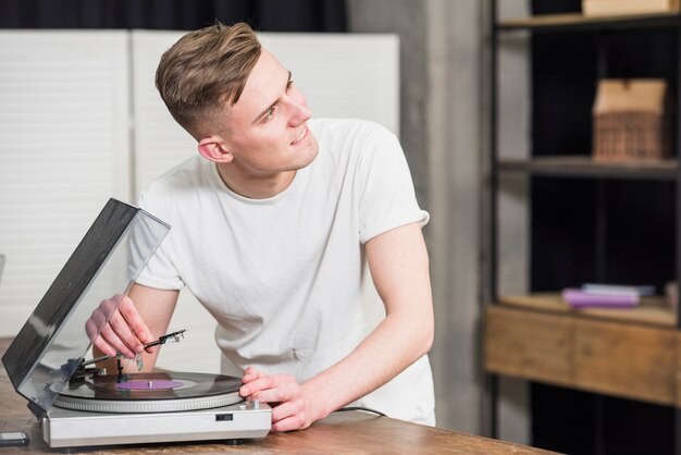 Happy young man while playing the turntable vinyl record player on the table looking away