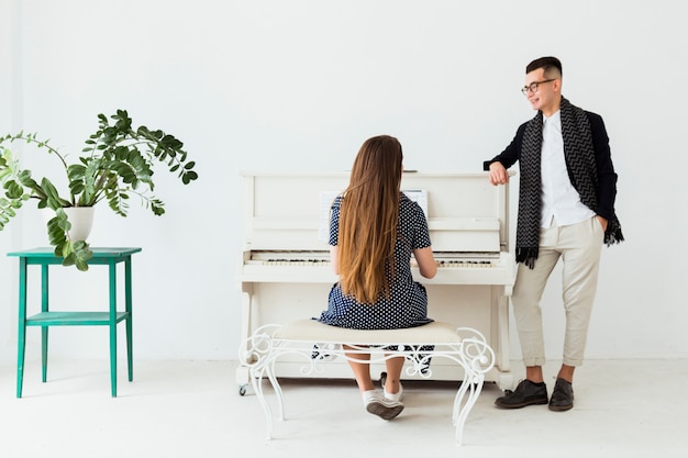 Happy young man with hand in her pocket looking at woman playing piano