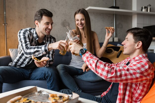 Happy young people eating pizza, drinking beer, having fun, friends party at home, hipster company together, two men one woman, smiling, positive, relaxed, hang out, laughing, 