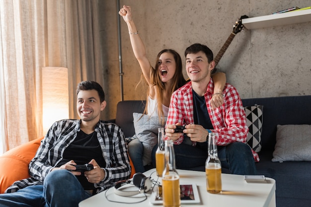 Free photo happy young people playing video games, having fun, friends party at home, hipster company together, two men one woman, smiling, positive, relaxed, emotional, laughing, competition