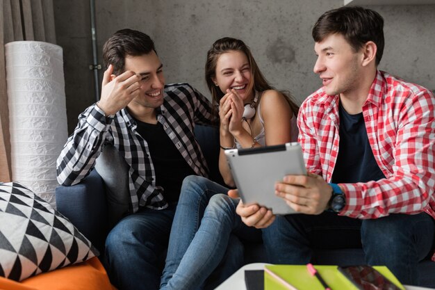 Happy young people using tablet, students learning, having fun, friends party at home, hipster company together, two men one woman, smiling, positive, online education, laughing