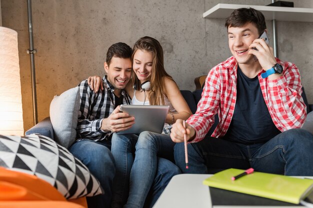 Happy young people using tablet, students learning, having fun, friends party at home, hipster company together, two men one woman, smiling, positive, online education, man talking on phone