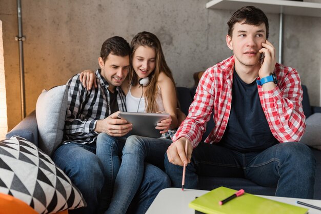 Happy young people using tablet, students learning, having fun, friends party at home, hipster company together, two men one woman, smiling, positive, online education, man talking on phone