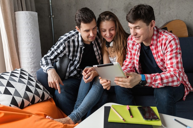 Happy young people using tablet, students learning, having fun, friends party at home, hipster company together, two men one woman, smiling, positive, online education