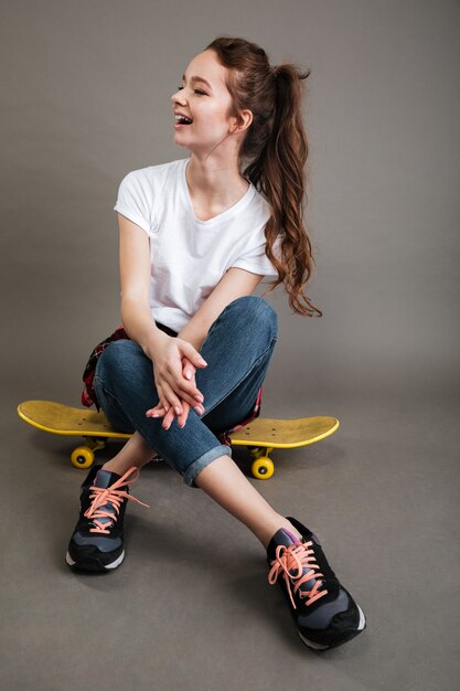 Happy young teenage girl sitting on skateboard and laughing