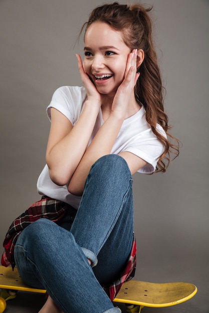 Happy young teenage girl sitting on skateboard and laughing