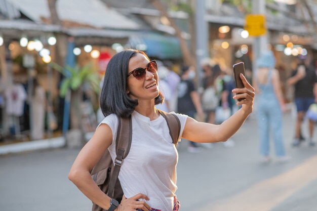 Happy young travel asian woman using mobile phone and relax on street.