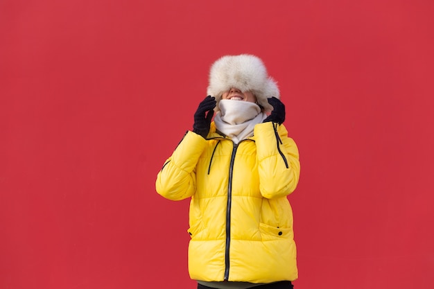 Free photo happy young woman on the background of a red wall in warm clothes on a winter sunny day