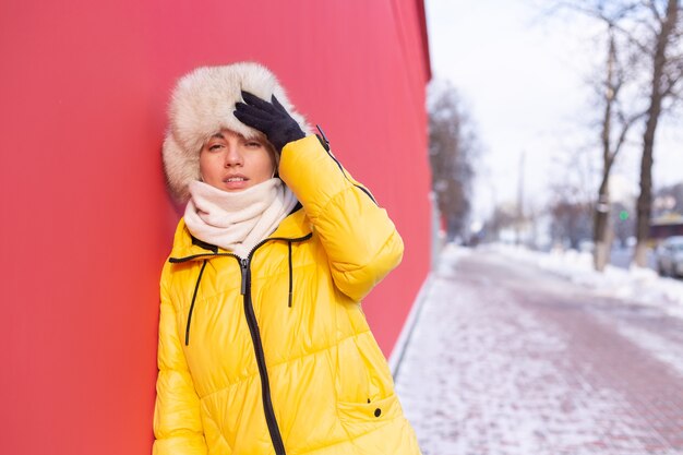 Happy young woman on the background of a red wall in warm clothes on a winter sunny day