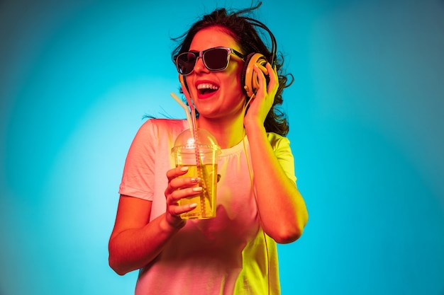 Happy young woman dancing and smiling in headphones over trendy blue neon studio