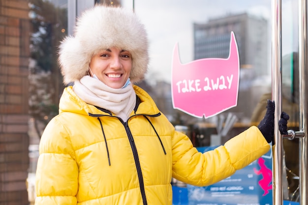 Happy young woman at the door of the restaurant on a cold winter day, lettering, takeaway food.