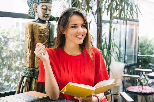 Happy young woman holding book in restaurant