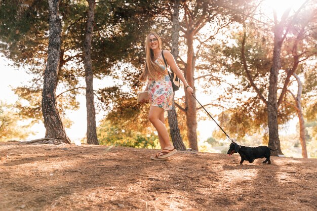 Happy young woman holding book walking with her dog in garden