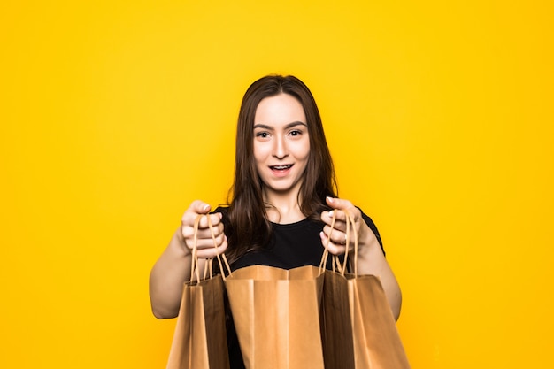 Happy young woman holding shopping bags on a yellow wall