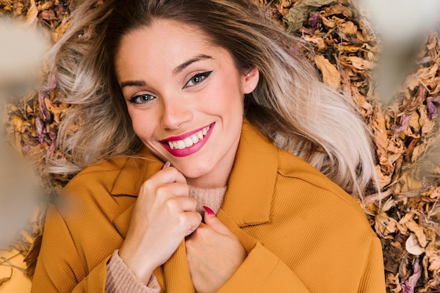 Happy young woman lying on dry leaves looking at camera