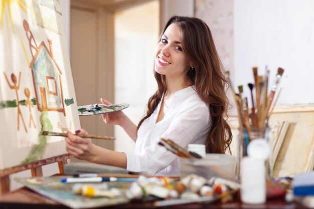 Happy young woman paints  on canvas