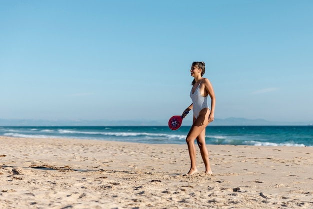 Free Photo happy young woman playing tennis on seashore