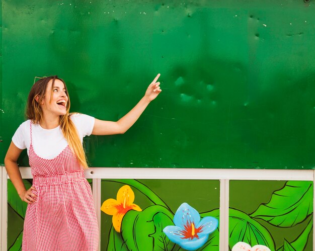 Happy young woman pointing finger on green wall