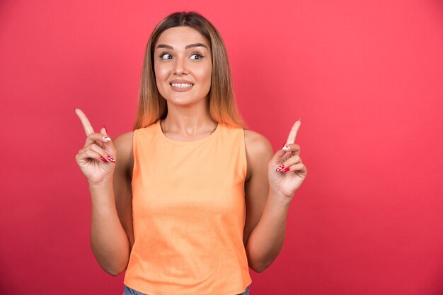 Happy young woman pointing her finger up on red wall. 