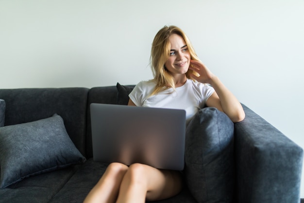 Happy young woman sitting on couch using her laptop at home in the living room