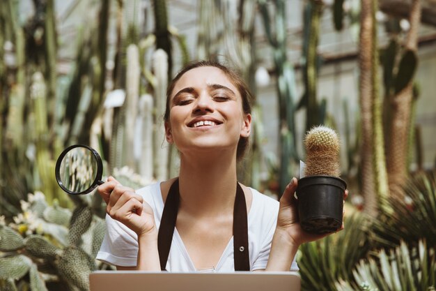 Happy young woman sitting in greenhouse using laptop